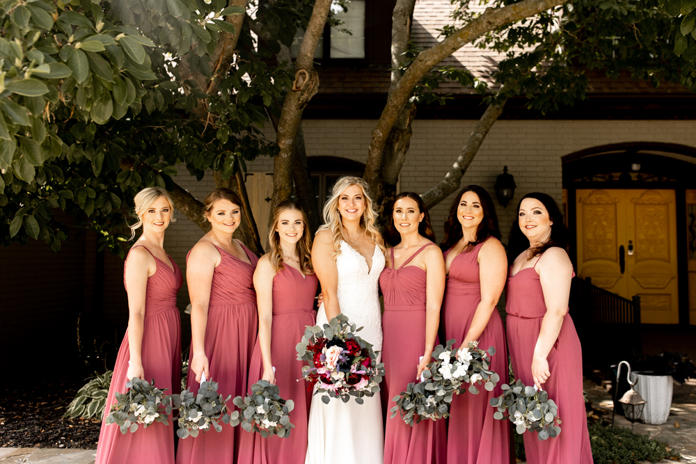 Bride and bridesmaids stand shoulder to shoulder outside of the Conrad Mansion for Iowa Wedding. 
