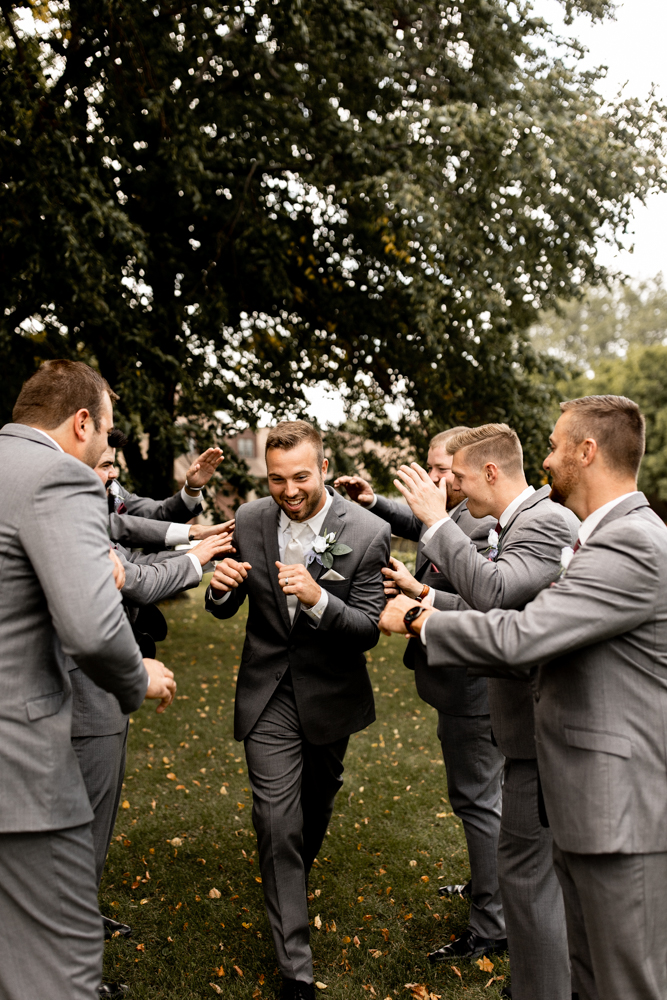 Groom walks through his groomsmen on either side as they have fun roughing him up.