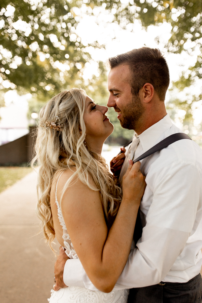 Bride pulls groom in by his suspenders for a kiss. Glowing couple happily in love and enjoying every moment of their wedding day. 