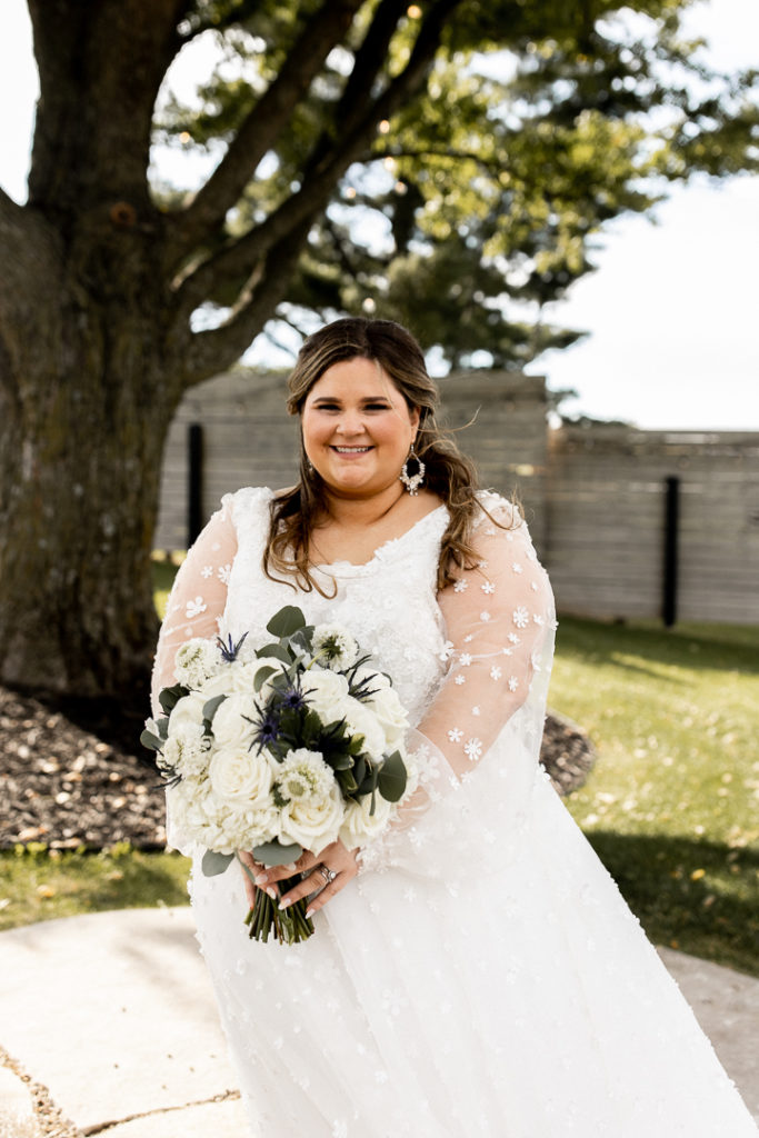 Bride poses for photos showcasing her beautiful long sleeve wedding dress, veil, and bridal bouquet in front of stunning background. Unforgettable wedding day moments captured by Iowa Wedding and Lifestyle Photographer. 