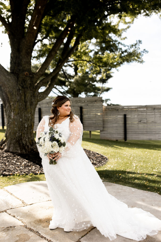 Bride poses for photos showcasing her beautiful long sleeve wedding dress, veil, and bridal bouquet. 
