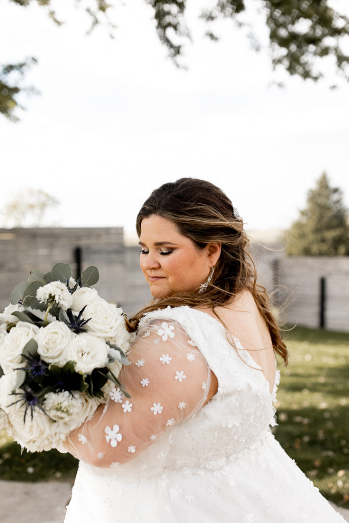 Bride peers over her shoulder and hangs her bouquet over her arm. Eyes closed in peaceful wedding pose. 