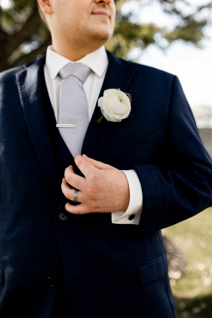 Close up shot of the groom showcasing the details of his suit, tie clip, and boutineer. 