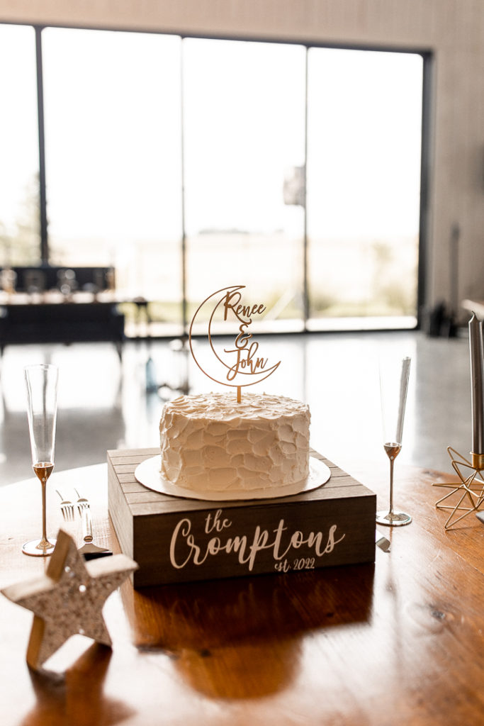 Beautiful cake and topper with a crescent moon and the name of the bride and groom. Sitting atop a wooden cake stand with their married last name! Gorgeous details photographed by Iowa Wedding Photographer. 