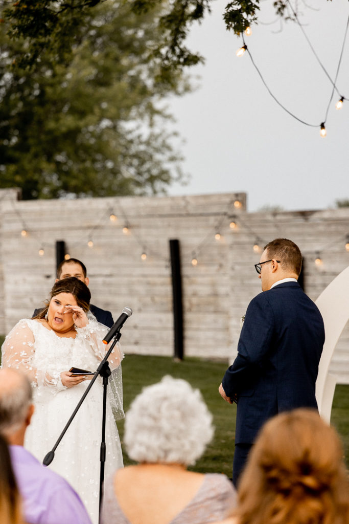 Bride pushes away tears as she becomes emotional reading her wedding vows she has written to her groom. Sweet emotions captured by Iowa Wedding Photographer. 