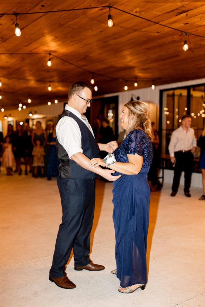 Groom shares a dance with his mom at the wedding reception. Little Lights on the Lane wedding venue offers stunning backgrounds with hanging lights completing the look!