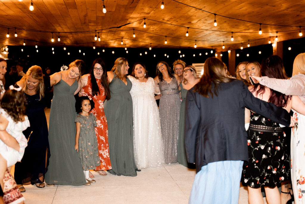 Hands over shoulders create a big circle on the dance floor as friends and family of the bride and groom come together to dance and celebrate the couple. Fun moments of the reception and wedding day captured by Iowa Wedding and Lifestyle Photographer. 