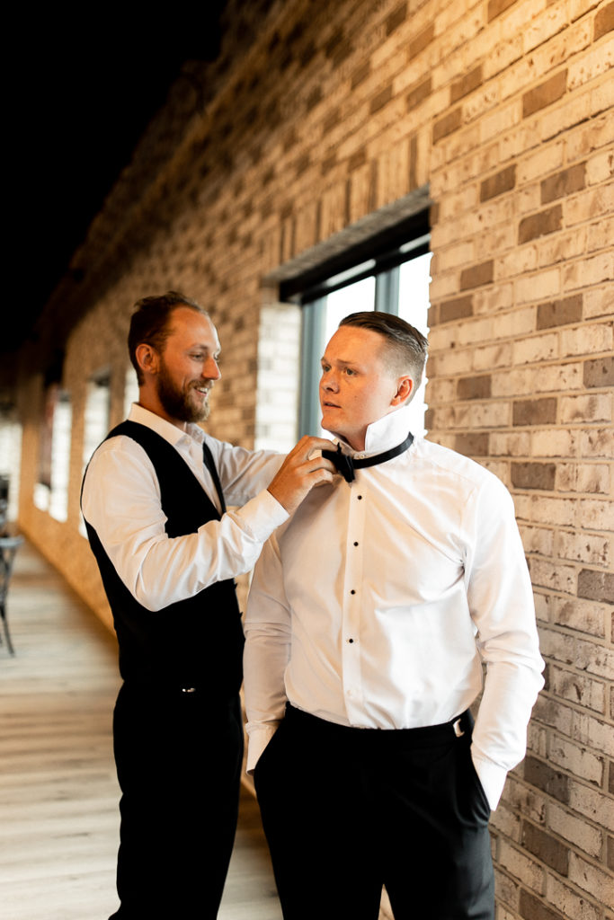 Groomsmen helps groom finish his wedding day look with his bowtie. 