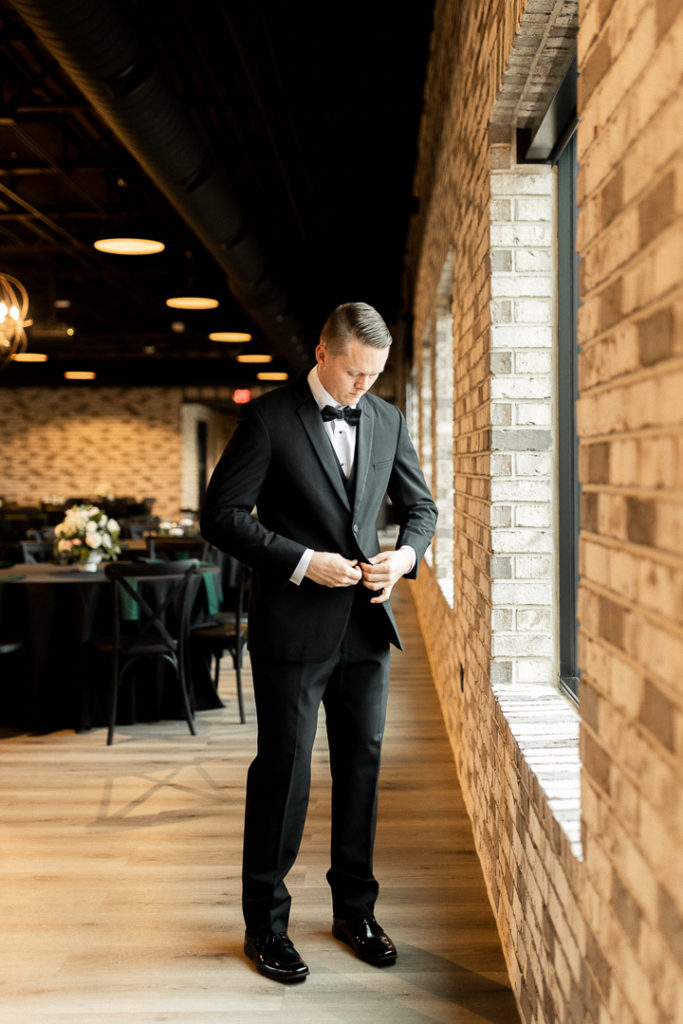Groom finishes buttoning his tux jacket as he prepares to see his bride for the first time on their wedding day. 
