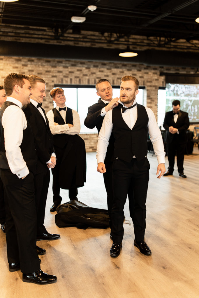 Groomsmen finish getting ready, helping each other with their bowties. Black tuxes looking sharp!
