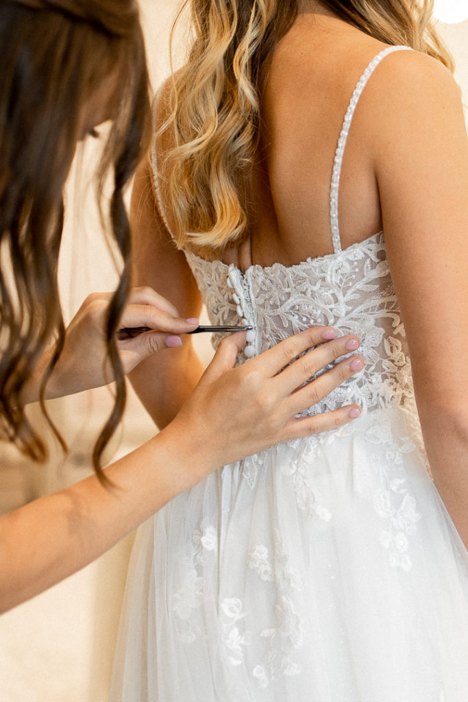 Bridesmaid uses hook to help bride button up her dress - finishing touches on the wedding dress!