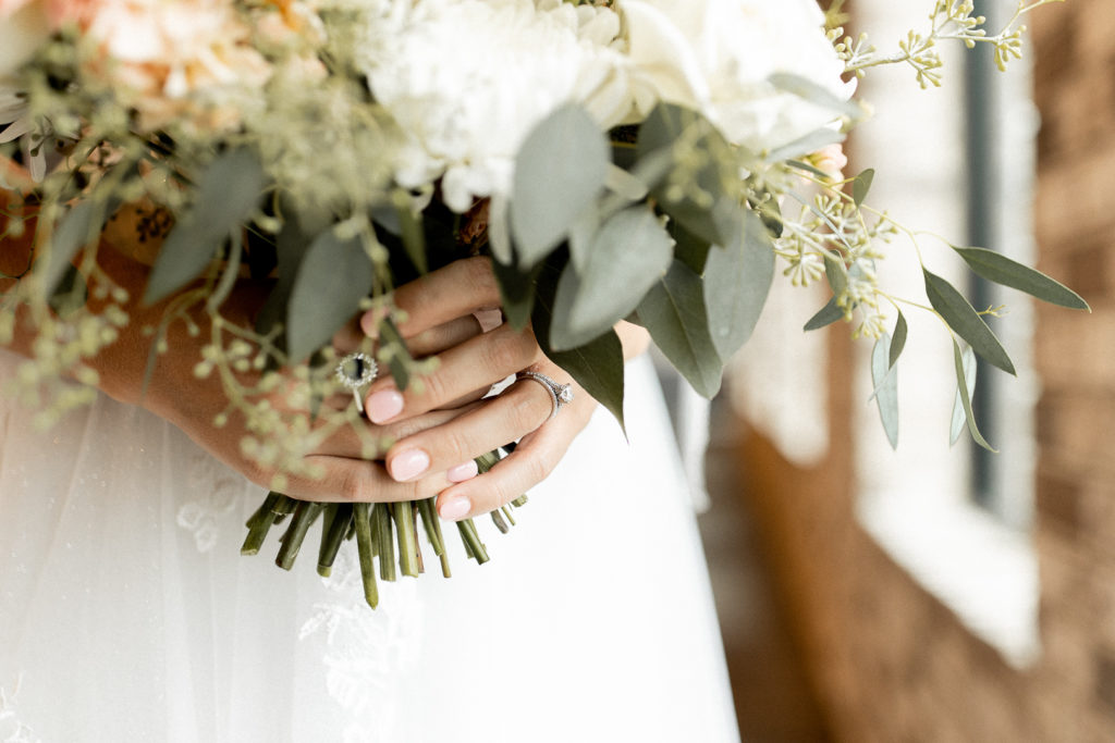 Detailed close up wedding photo showcasing wedding ring and greenery of brides floral bouquet. 