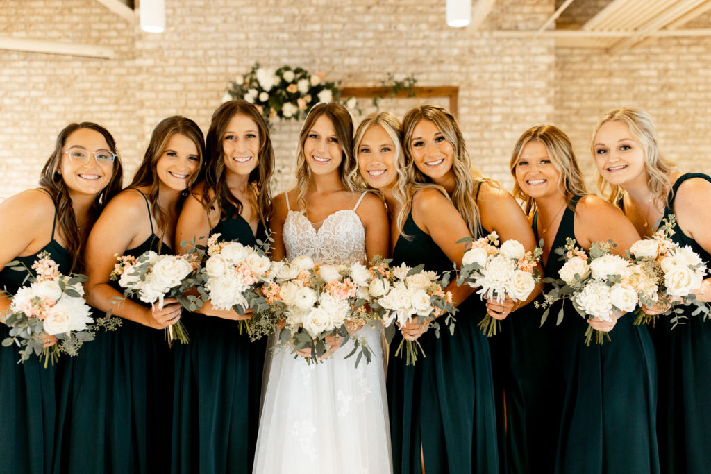Bride and bridesmaids get in nice and cozy for a photo. Royal green bridesmaid dresses pairing beautifully with their wedding day bouquets. 