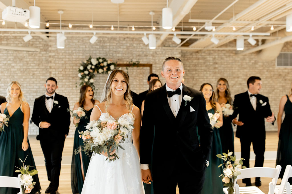 Bride and groom hold hands and smile for the Iowa Wedding Photographer as the rest of their wedding party walk behind them and smile. 