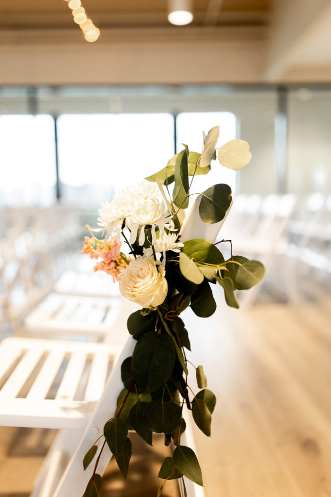 Simple yet stunning greenery and florals hang from the back of the chair as sweet decoration at this Iowa Wedding Venue - Toast. Captured by talented Iowa Wedding Photographer. 