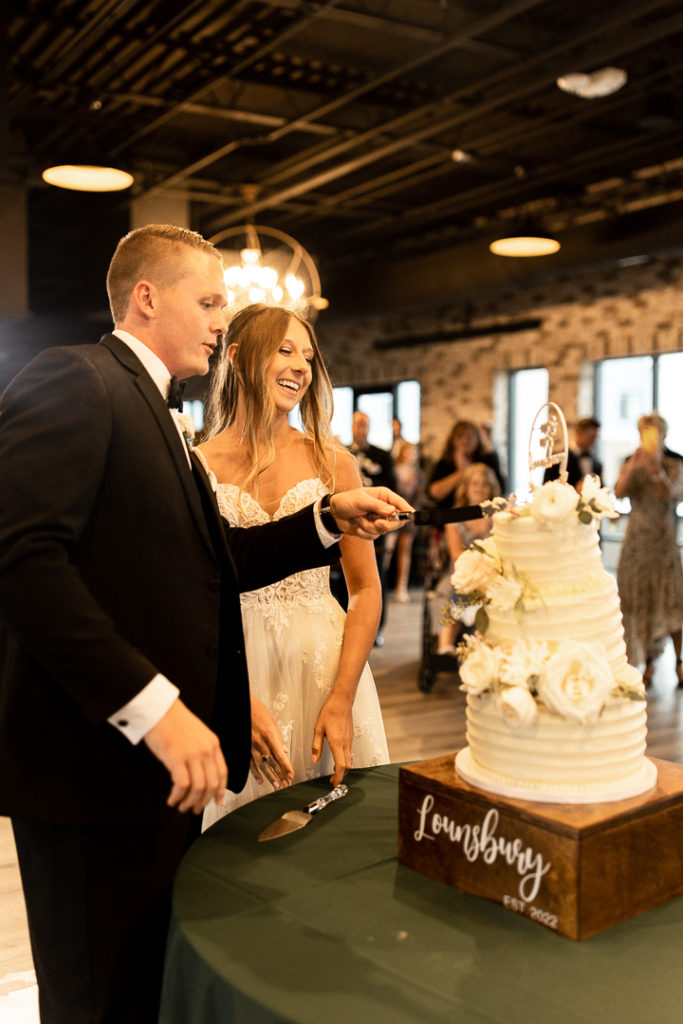 Bride and groom are beaming with joy as they enter their wedding reception and cut their cake. Captured by Iowa and Midwest Wedding Photographer. 