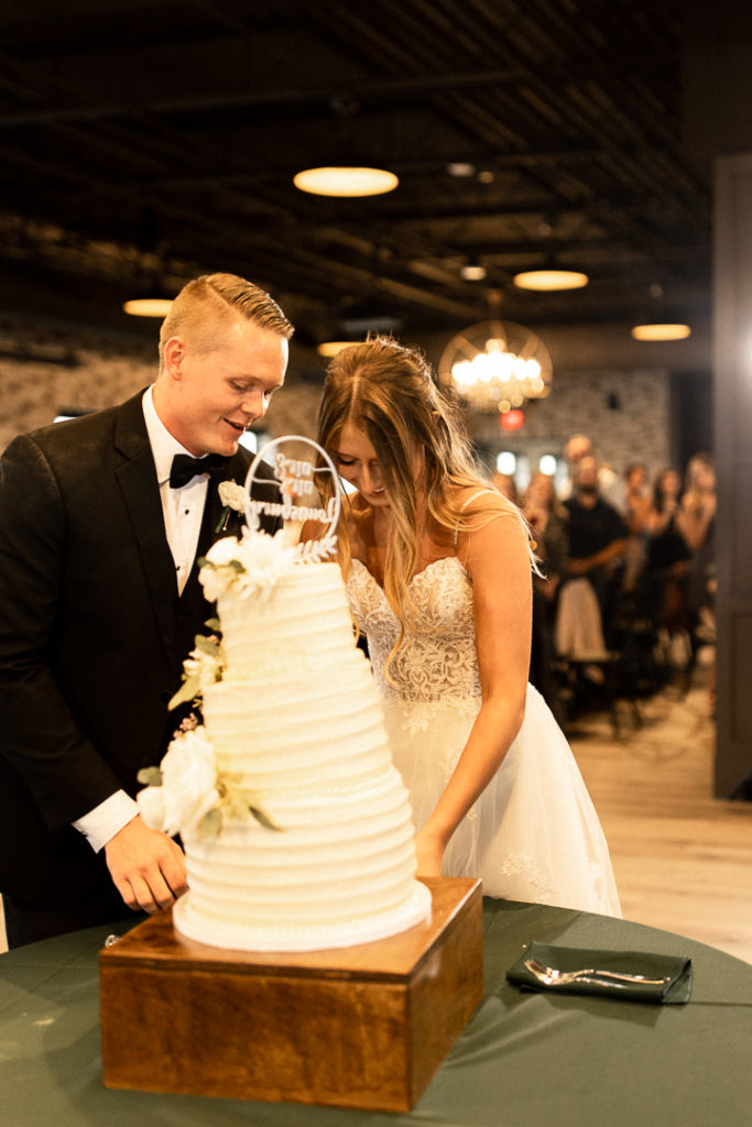 Husband and wife have cut their three tiered wedding cake and are about to give each other their bites. Smiles light up their faces in pure joy at their wedding ceremony in Ankeny Iowa at Wedding Venue Toast. 