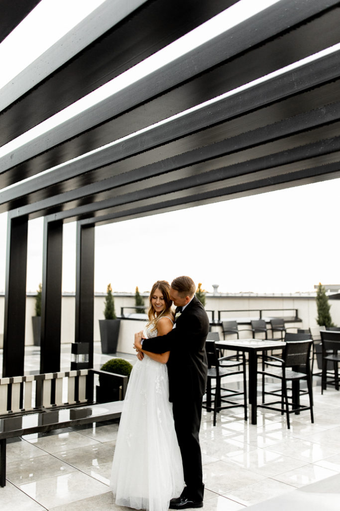 Bride and groom pose for their photographer with black iron patio structure around them. Stunning high structure and all black pairs perfectly with groom's black tuxedo leaving the bride standing out in white wedding dress. 