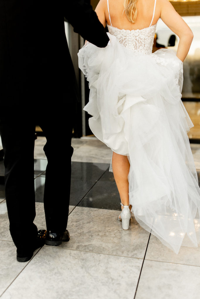 Sweet moments captured by this Iowa Wedding Photographer. Photo caught from behind as bride pulls her wedding dress train up and holds it in her right arm as her left is escorted by her now husband. Beautiful black and white sharp colors contrasting nicely. 