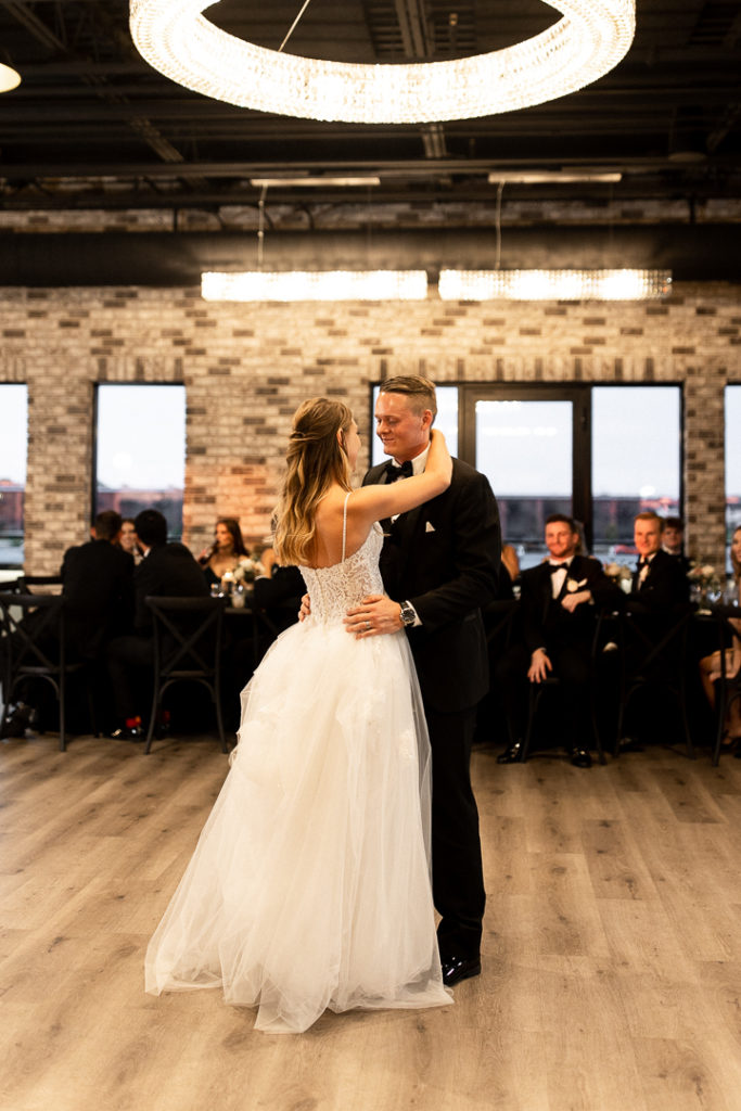 Bride and groom share their first dance as husband and wife with beautiful light fixture hanging above them at stunning Iowa Wedding Venue Toast in Ankeny Iowa. Sweet moments and memories captured by Iowa and Midwest Wedding Photographer. 