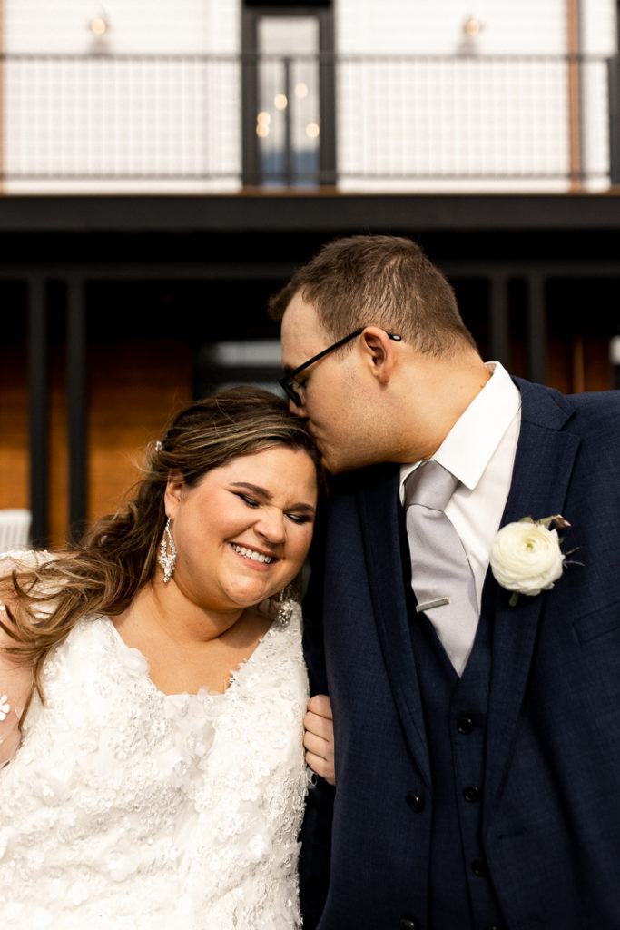 Groom kisses his bride's head and a huge joyful smile fills her entire face. 