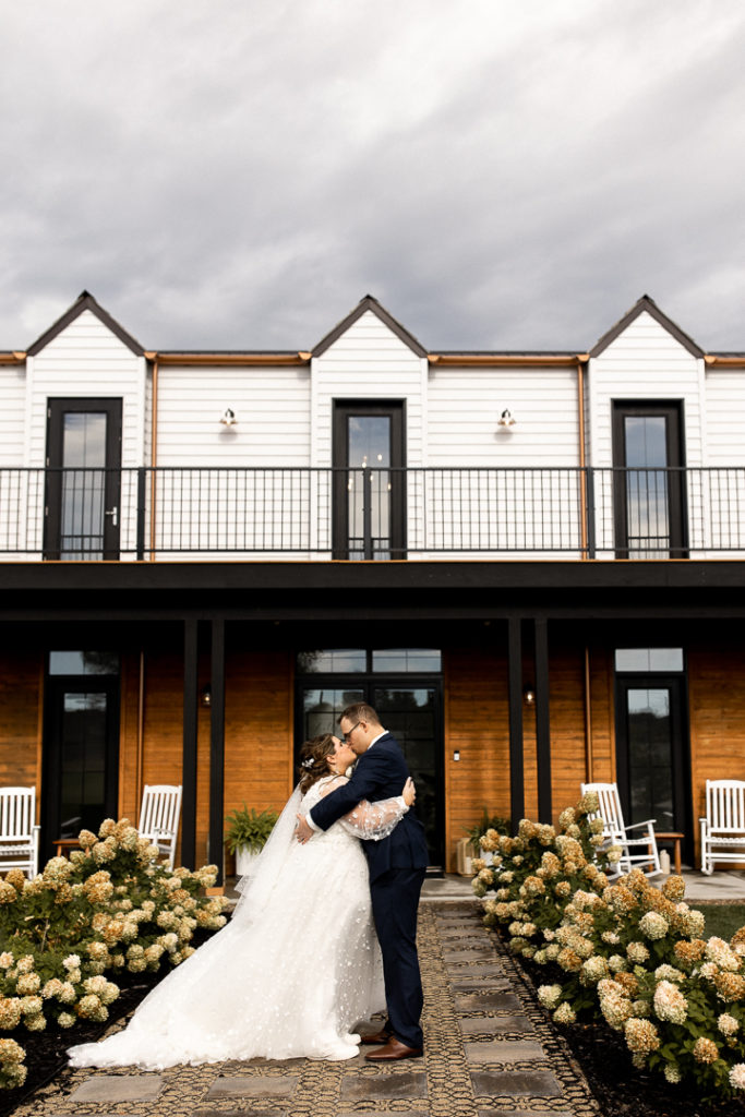 Husband and wife pose in front of their beautiful wedding venue space - Little Lights on the Lane. Gorgeous venue and background for wedding photos! 